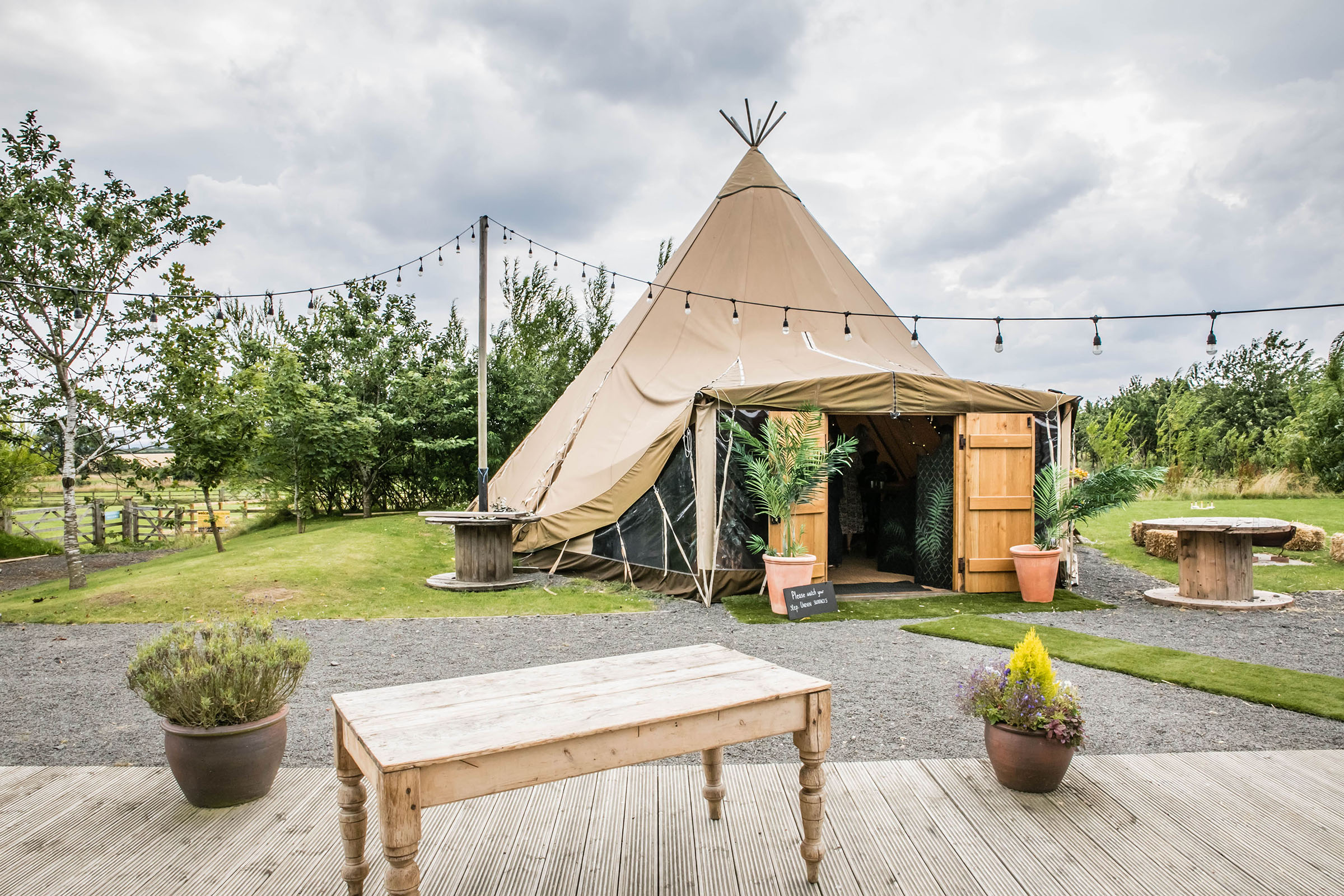 Nordic-style tipi marquee set amidst the scenic countryside at Vallum Weddings, featuring rustic outdoor décor, festoon lights, and a welcoming sign—ideal for relaxed, boho-inspired wedding celebrations in Northumberland.